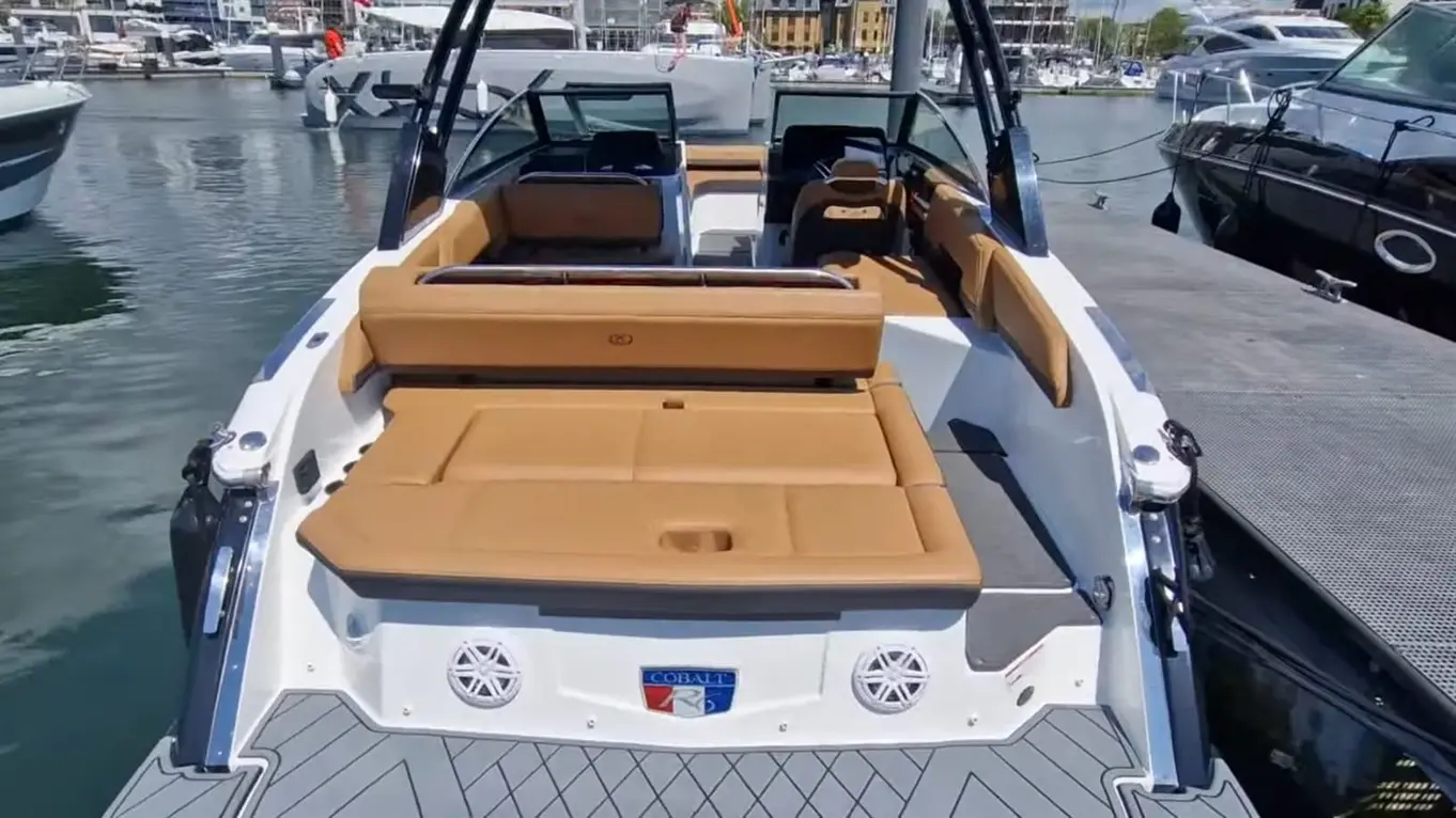 A luxury boat with tan seating and Cobalt branding docked at a marina, surrounded by other boats and a clear blue sky.